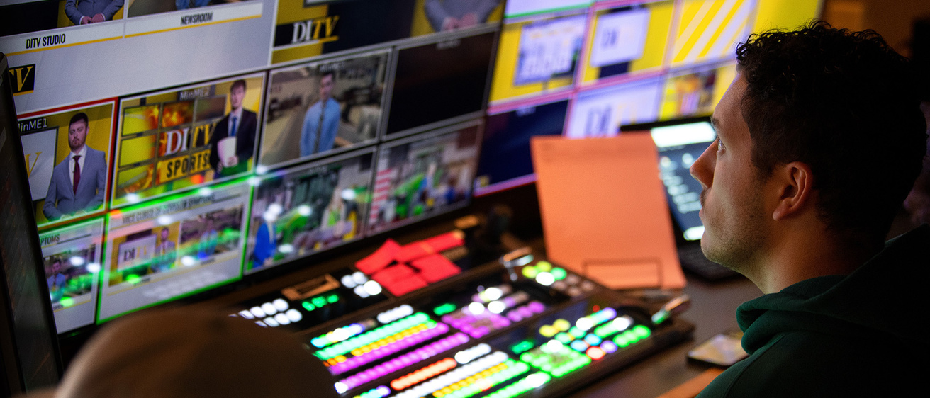 a producer in a broadcast booth, looking at numerous screens