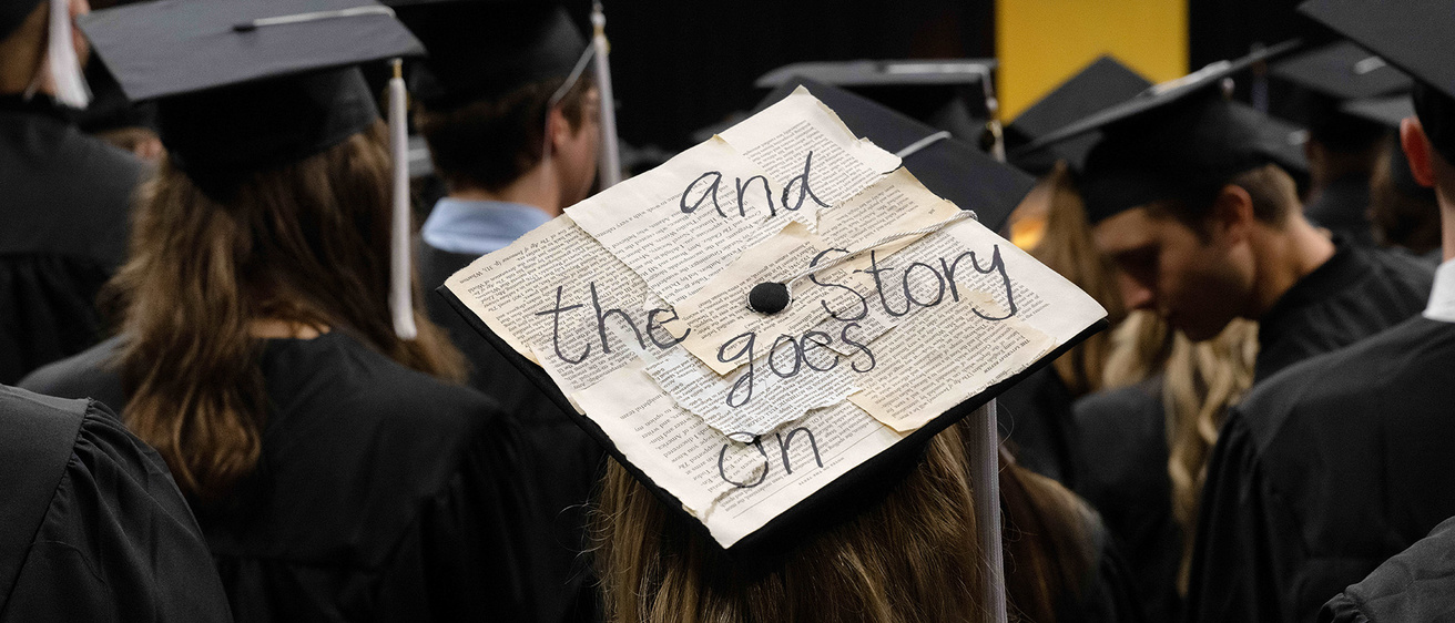 a graduation cap with excerpts of writing affixed to it, with an overarching message of "and the story goes on" written large in marker