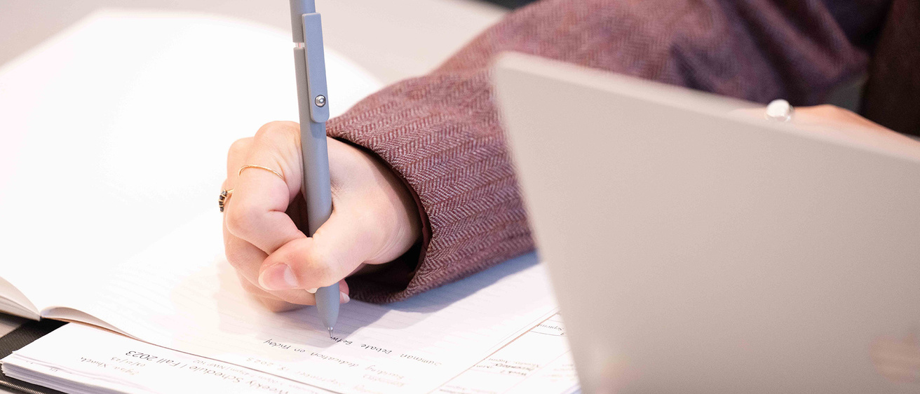 a person writing notes with a laptop nearby
