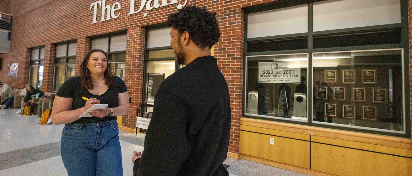 two people speaking outside of a college newspaper newsroom