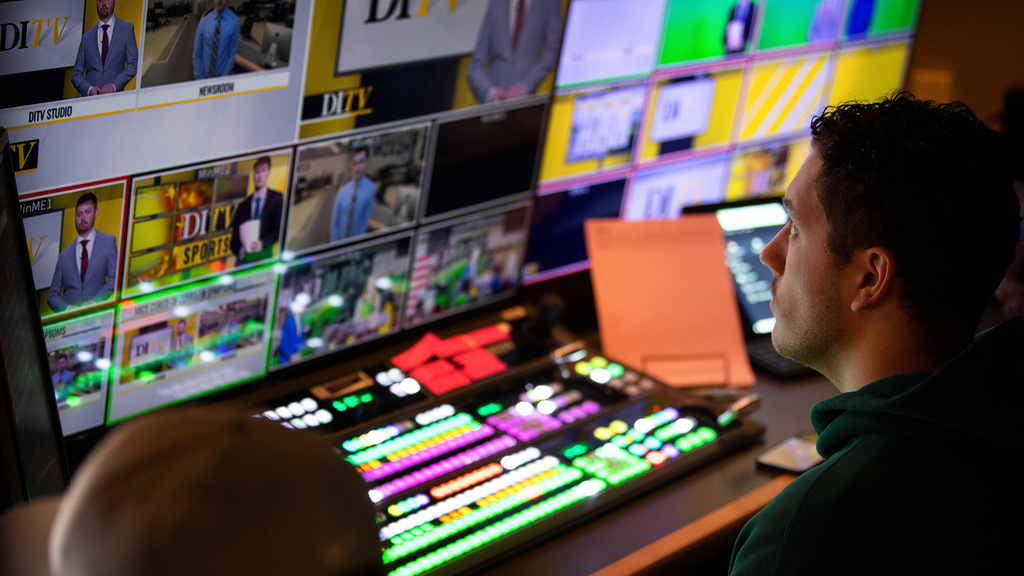 a producer in a broadcast booth, looking at numerous screens