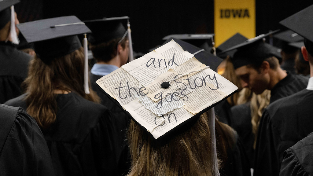 a graduation cap with excerpts of writing affixed to it, with an overarching message of "and the story goes on" written large in marker