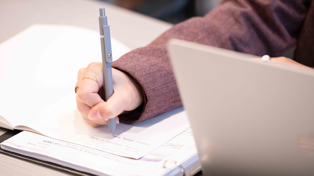 a person writing notes with a laptop nearby