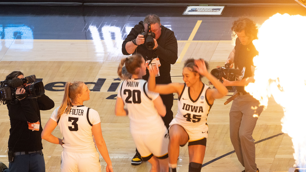 a photographer working at a college basketball game, shooting photos of two players hip-checking each other during lineup announcements